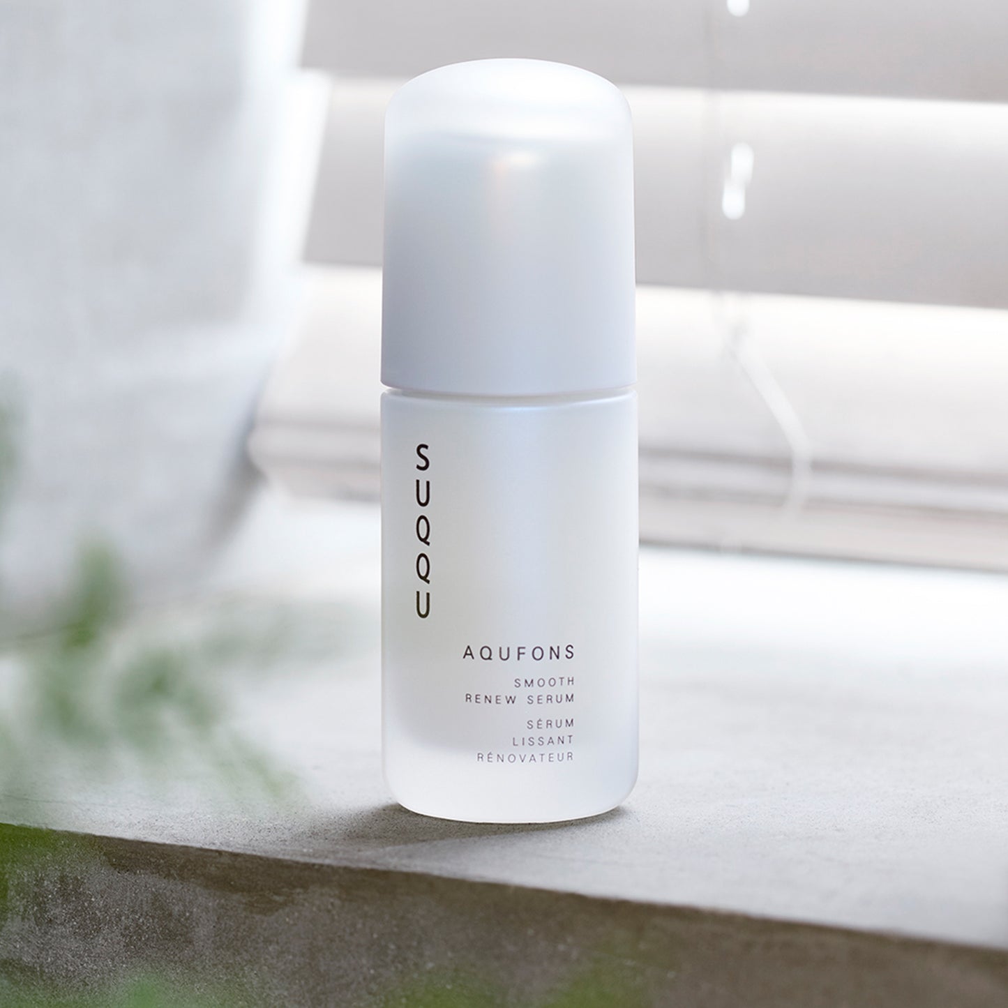 SUQQU Aqufons Smooth Renew Serum skincare bottle on window sill.