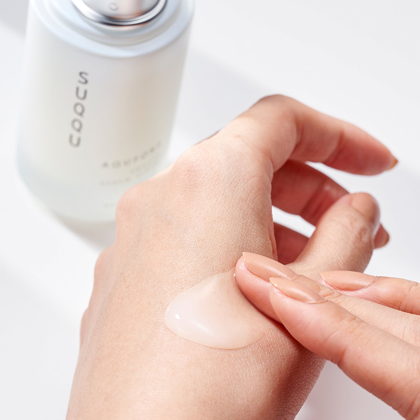 SUQQU Aqufons Smooth Renew Serum skincare bottle with creamy texture being applied to the back of a hand.