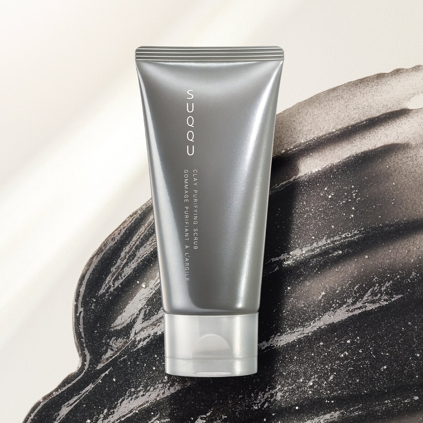 SUQQU Clay Purifying Scrub luxury Japanese face cleansing skincare product tube on dark clay scrub texture background.