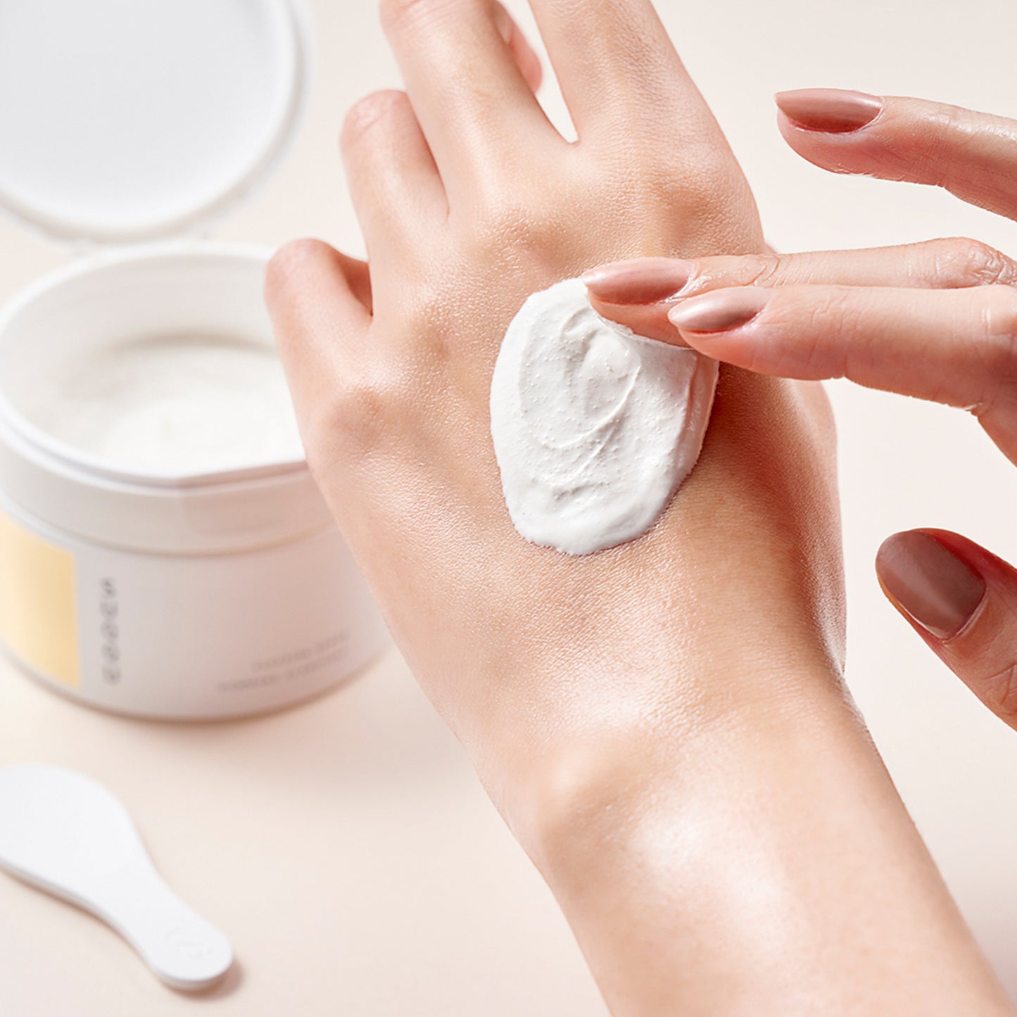 SUQQU Clearing Scrub tub open with luxurious cleansing scrub texture shown on hand.