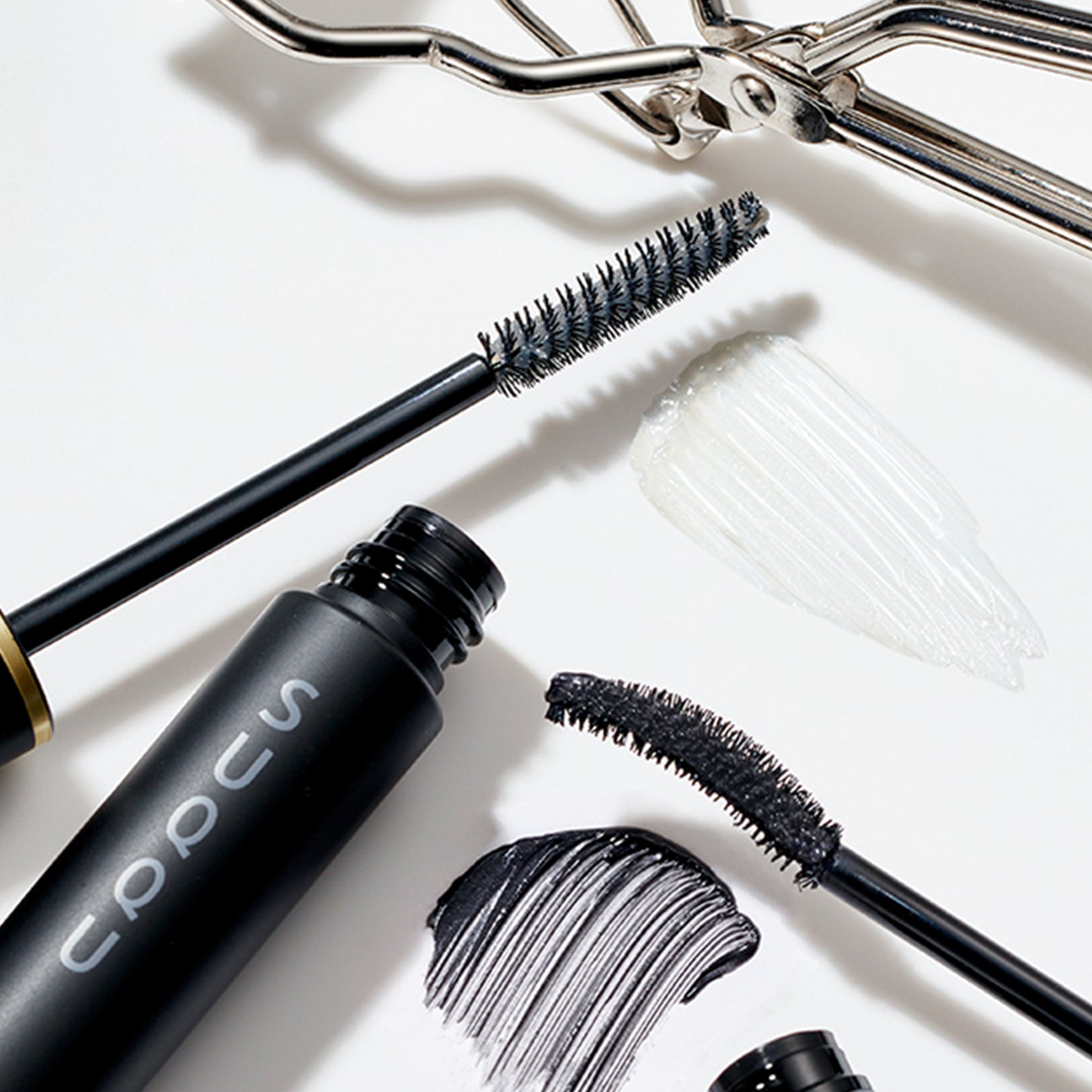 SUQQU Defining Eyelash Base with wand and texture on a table with other eyelash products.