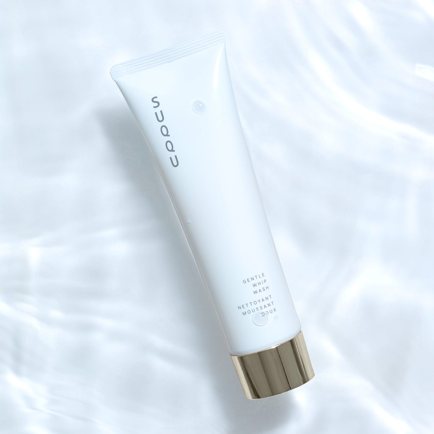 SUQQU Gentle Whip Wash luxury foaming face cleansing skincare product tube on water ripple background.