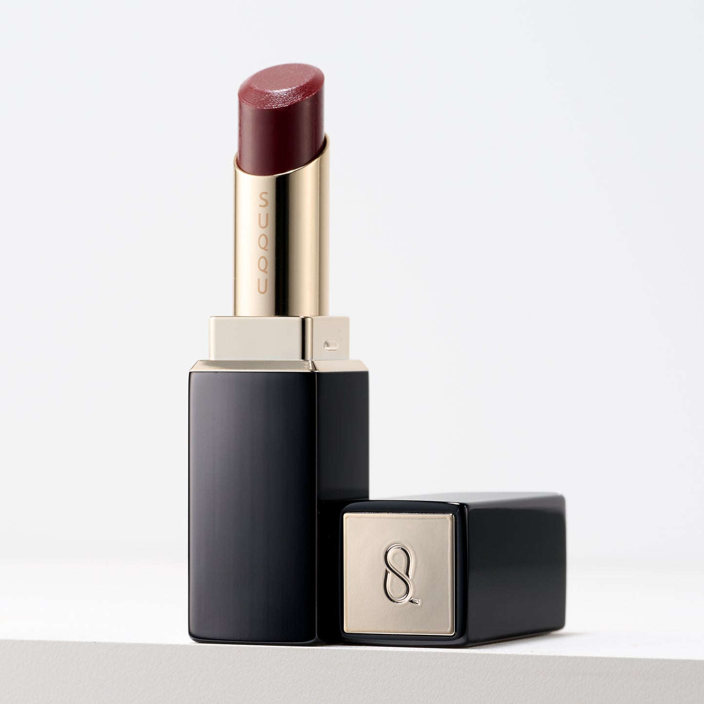 SUQQU Moisture Glaze Lipstick Japanese luxury colour make up with lip care ingredients and glazed finish with case and cap on table.