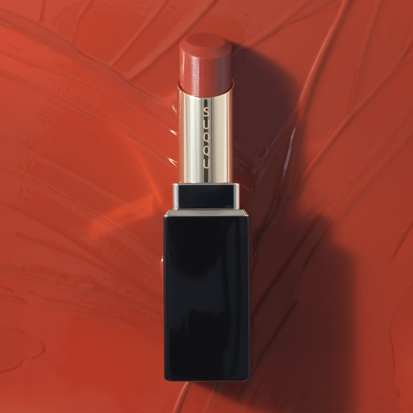 Orange Red SUQQU Moisture Glaze Lipstick on bright liquid colour background.