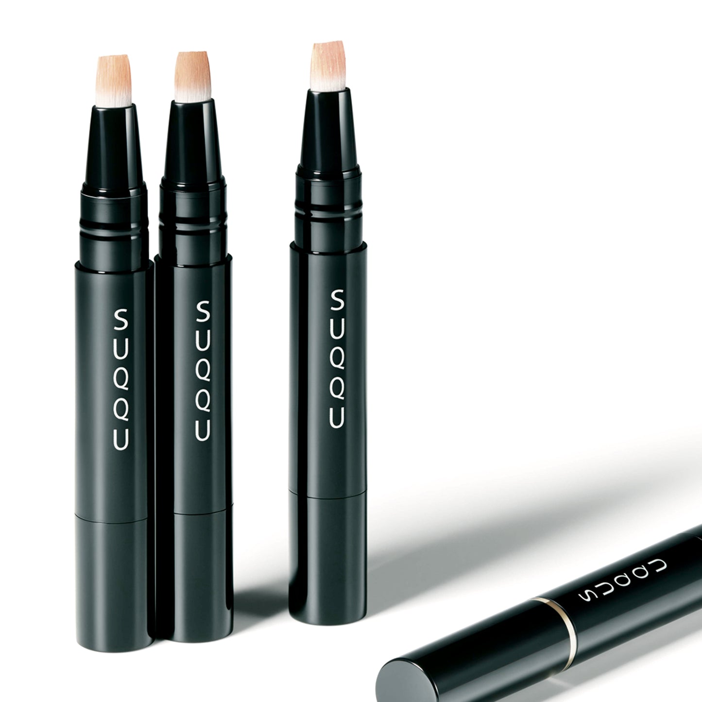 Three open SUQQU Radiant Cream Concealer base make up products on plain background plus one lying down with cap.