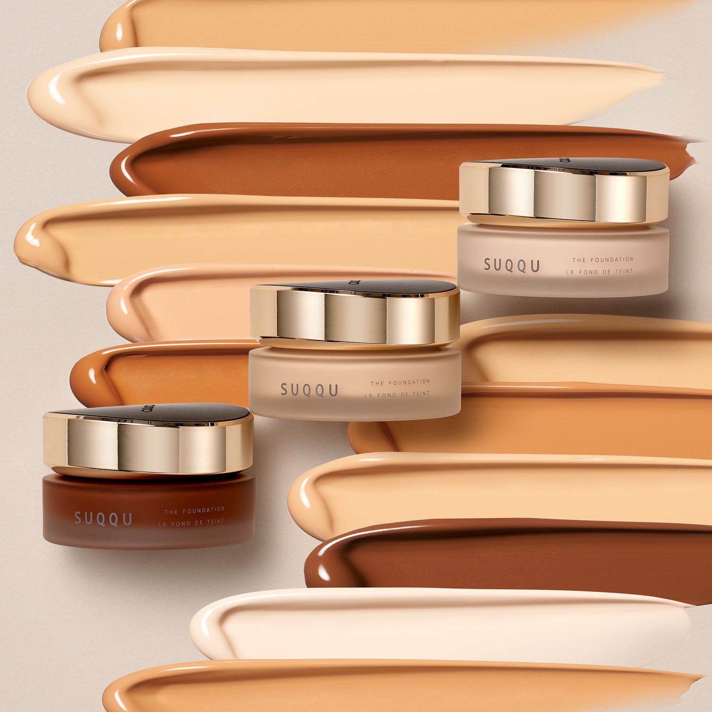 Three SUQQU The Foundation luxury moisturising Japanese cream base make up jars with cream swatch background.
