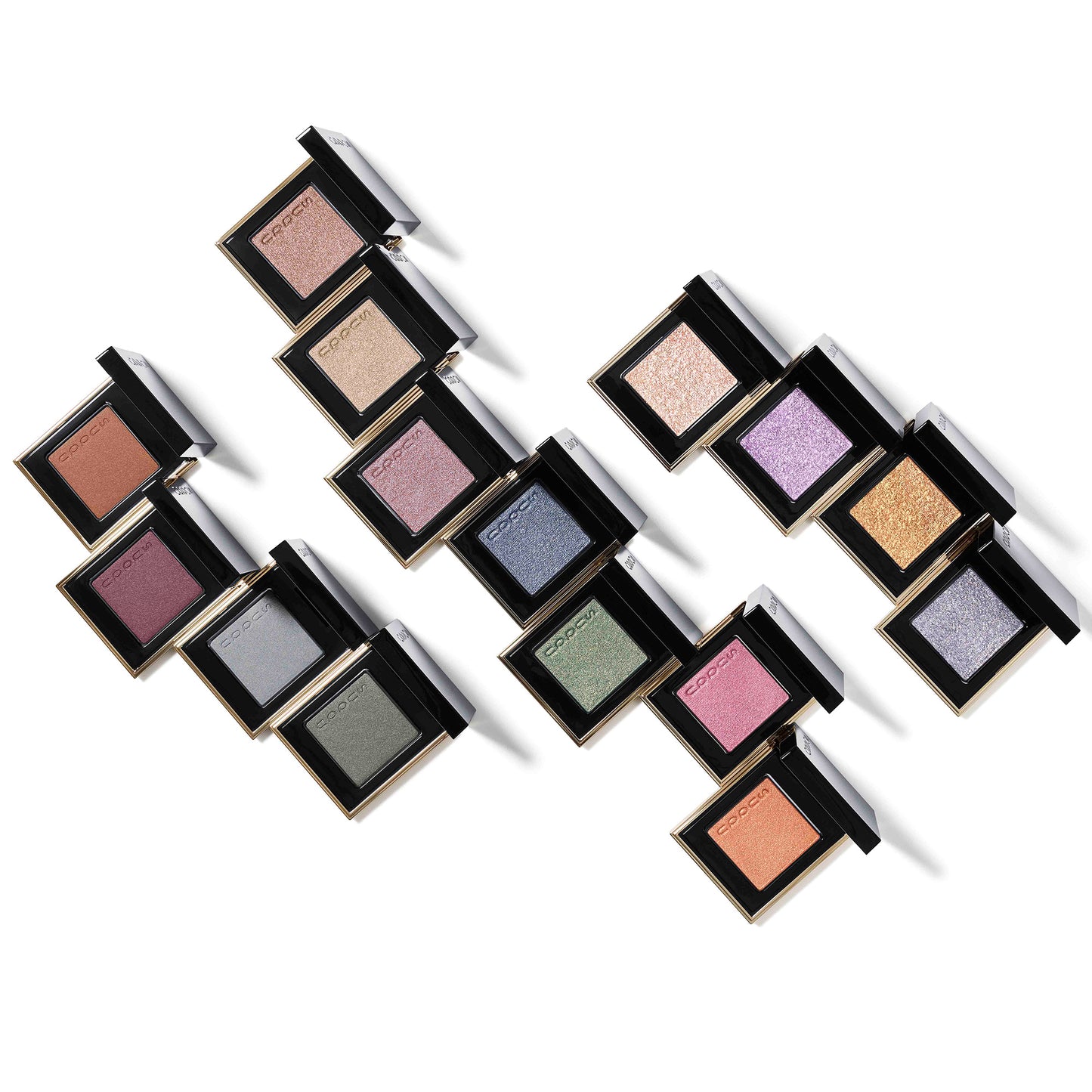 Multiple colourful SUQQU Tone Touch Eyes single eyeshadow make up palette products with lid open on plain background.