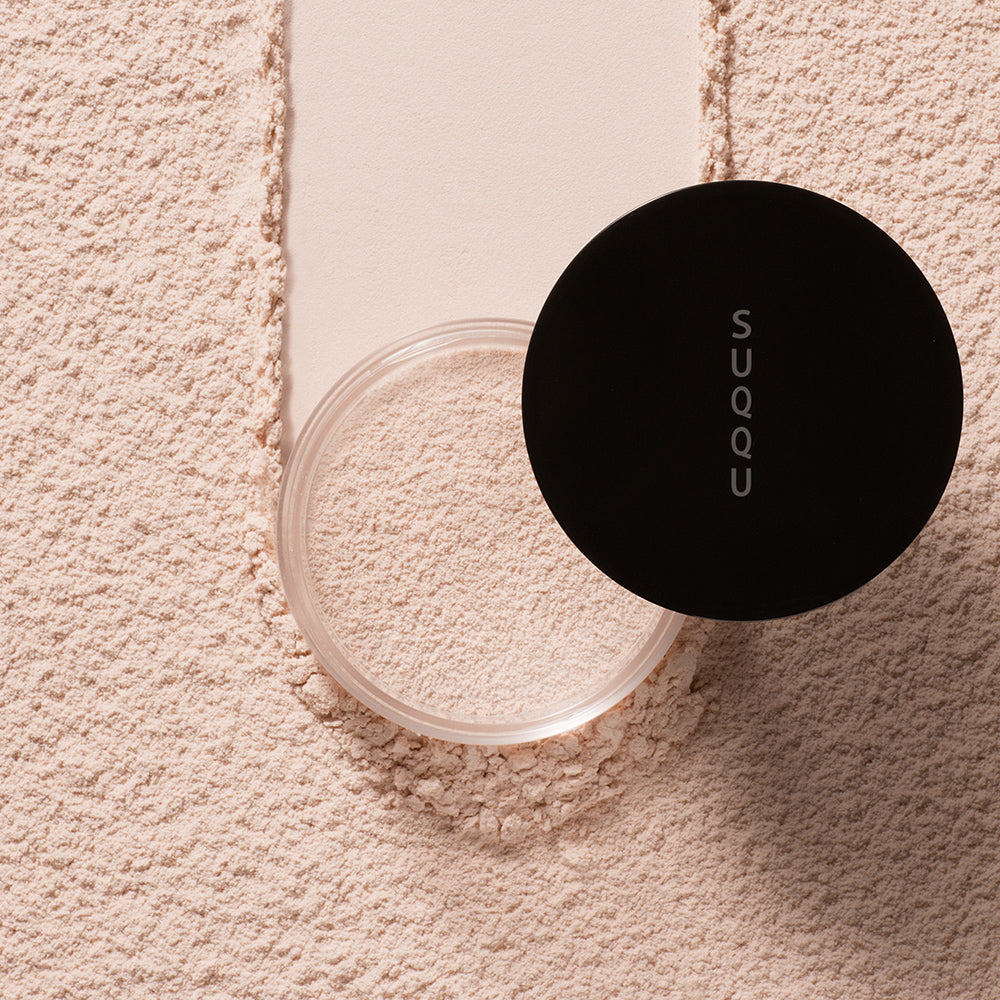 SUQQU Oil Rich Glow Loose Powder e face powder pot on powdery texture background.