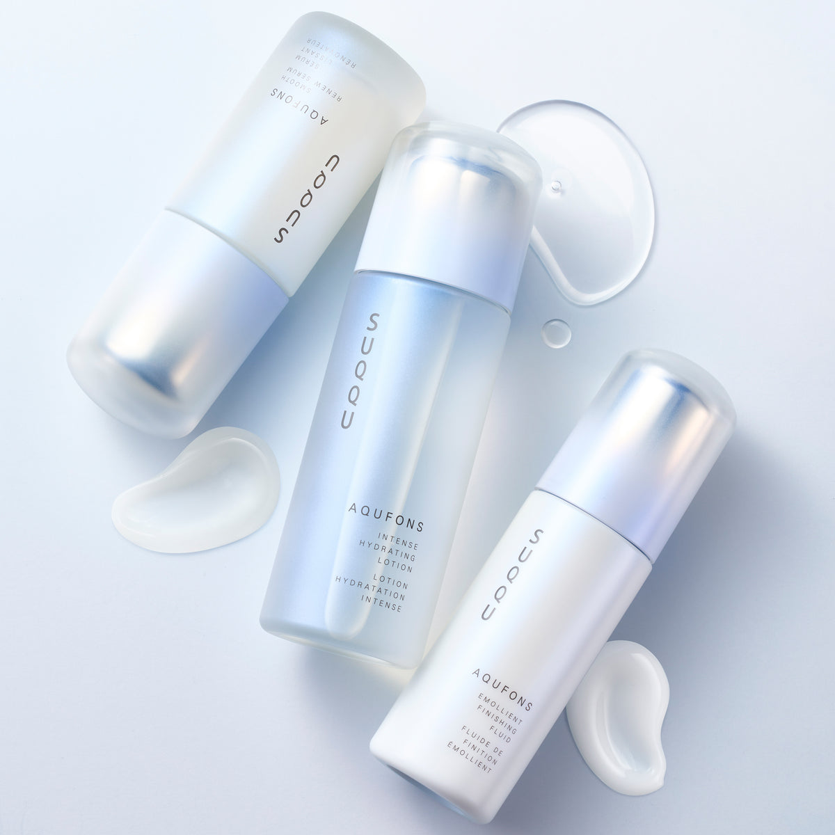 SUQQU Aqufons Intense Hydrating Lotion, Aqufons Emollient Finishing Fluid and Aqufons Smooth Renew Serum skincare moisturiser pump bottles on blue background with liquid and cream texture swatches.