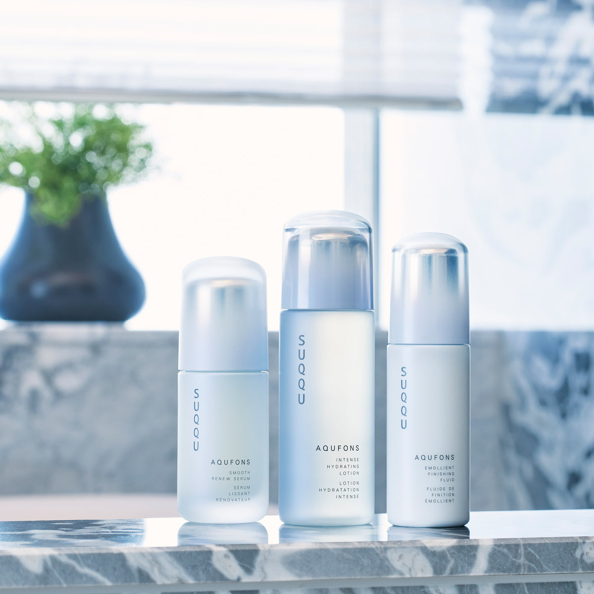 Three skincare products from SUQQU's 'Aqufons' range standing in a line on a bathroom table. Serum, lotion and fluid face moisturisers in pump bottles.
