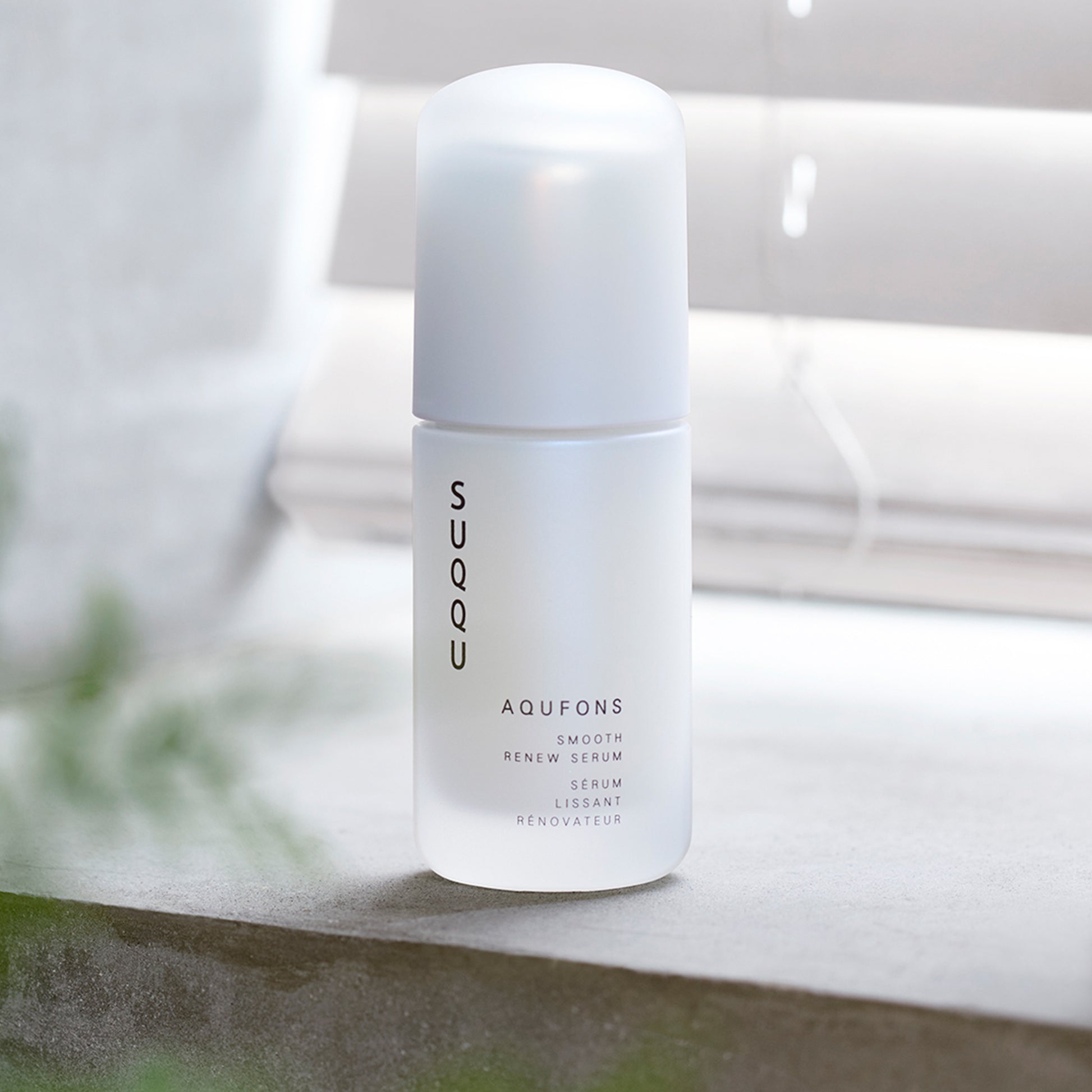 SUQQU Aqufons Smooth Renew Serum skincare bottle on window sill.
