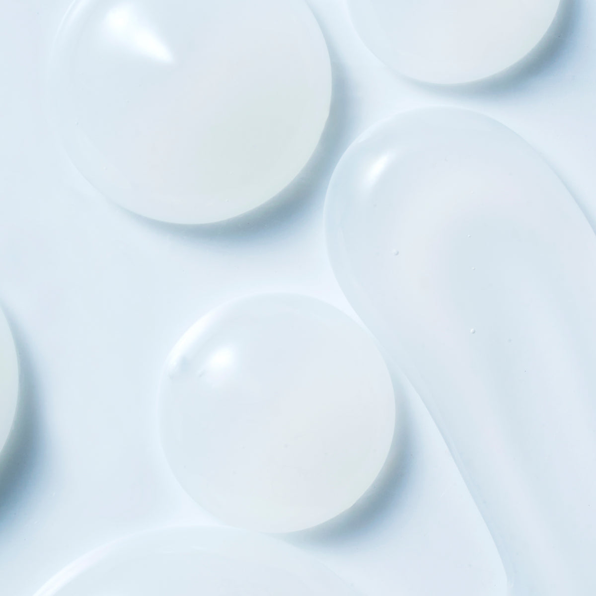 SUQQU Aqufons Water Tuning Gel face moisturiser gel texture dots on pale blue background, showing the gel like texture that feels like a hydrating watery veil when applied to skin.