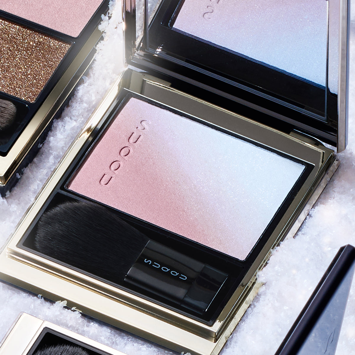 SUQQU Blurring Color Blush 118 open black and gold luxury blusher compact on snowy background. Soft pink and pale blue highlighter shades.