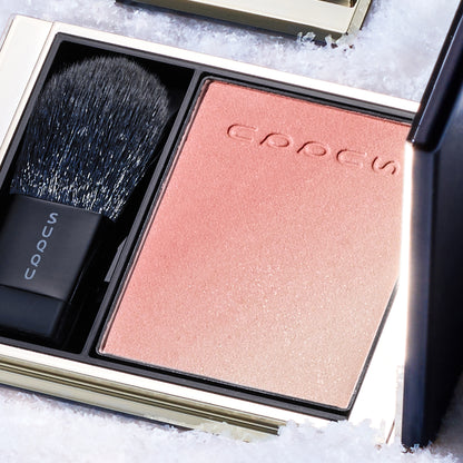 SUQQU Blurring Color Blush 119 open black and gold luxury blusher compact on snowy background. Coral pink and pale beige pink highlighter shades.
