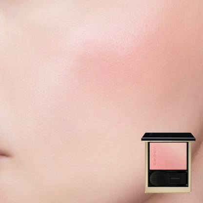 SUQQU Blurring Color Blush 119 luxury Japanese cosmetic blusher compact shown with model cheek wear close up background. Coral pink and pale beige pink highlighter shades.
