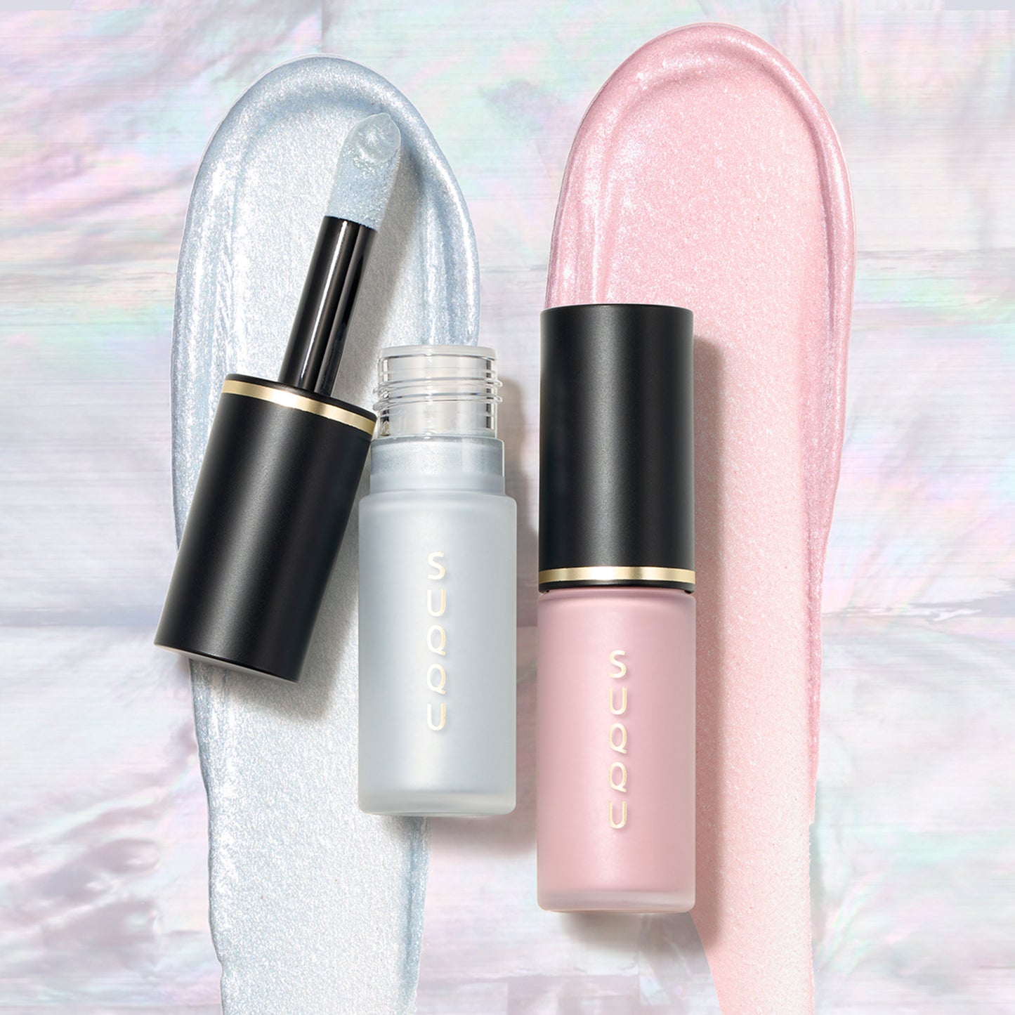 SUQQU Complexion Face Color 06 and 102 liquid highlighter blushers with applicator wand. Displayed on soft shimmering pink and blue pearlescent texture swatch background.