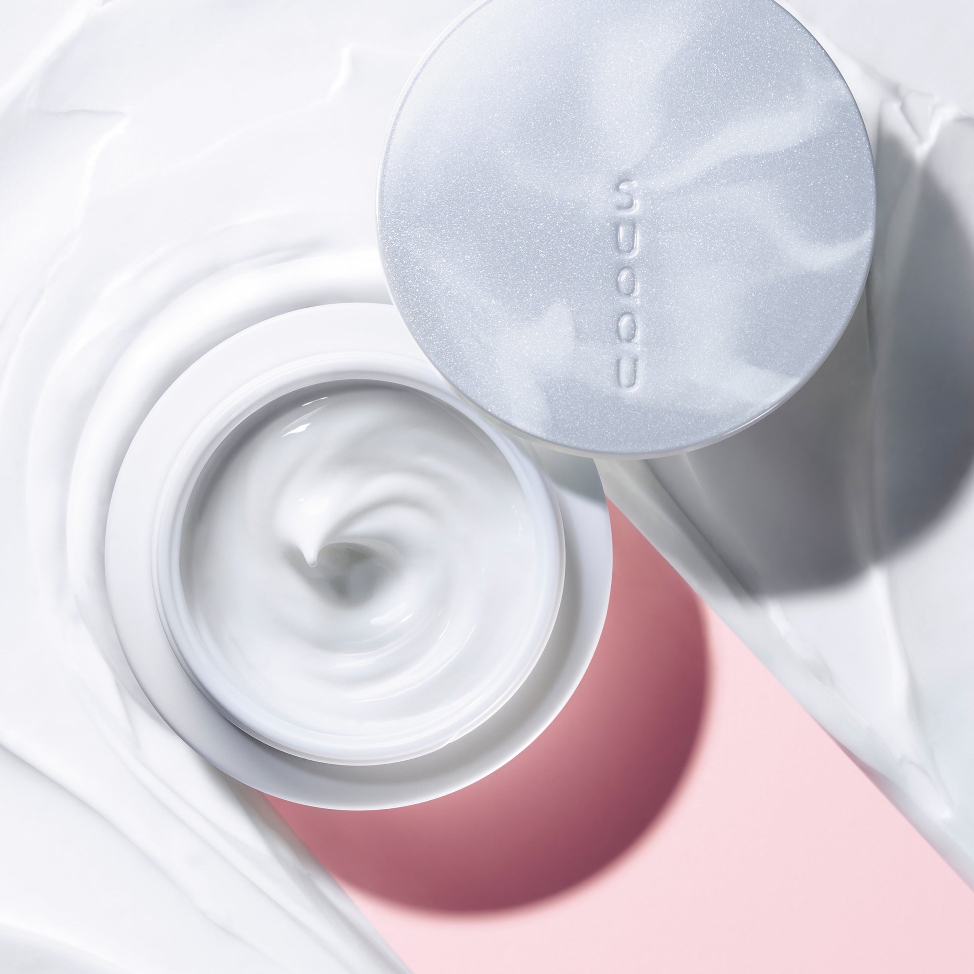 SUQQU Designing Massage Cream skincare product tub open on creamy background.