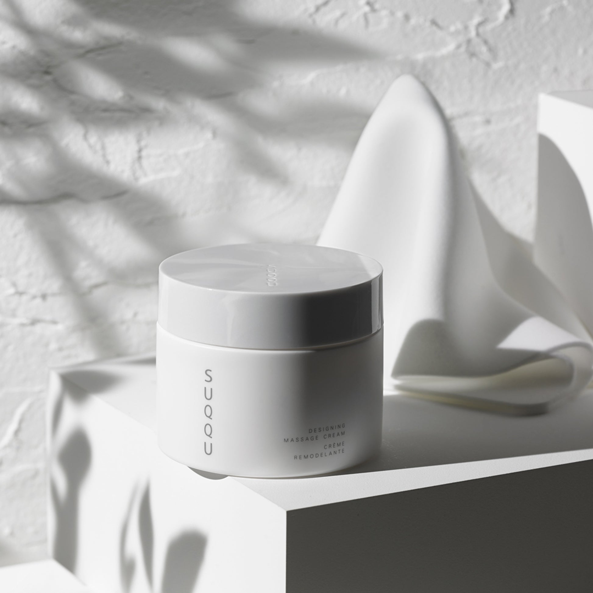 SUQQU Designing Massage Cream tub with cloth in background.