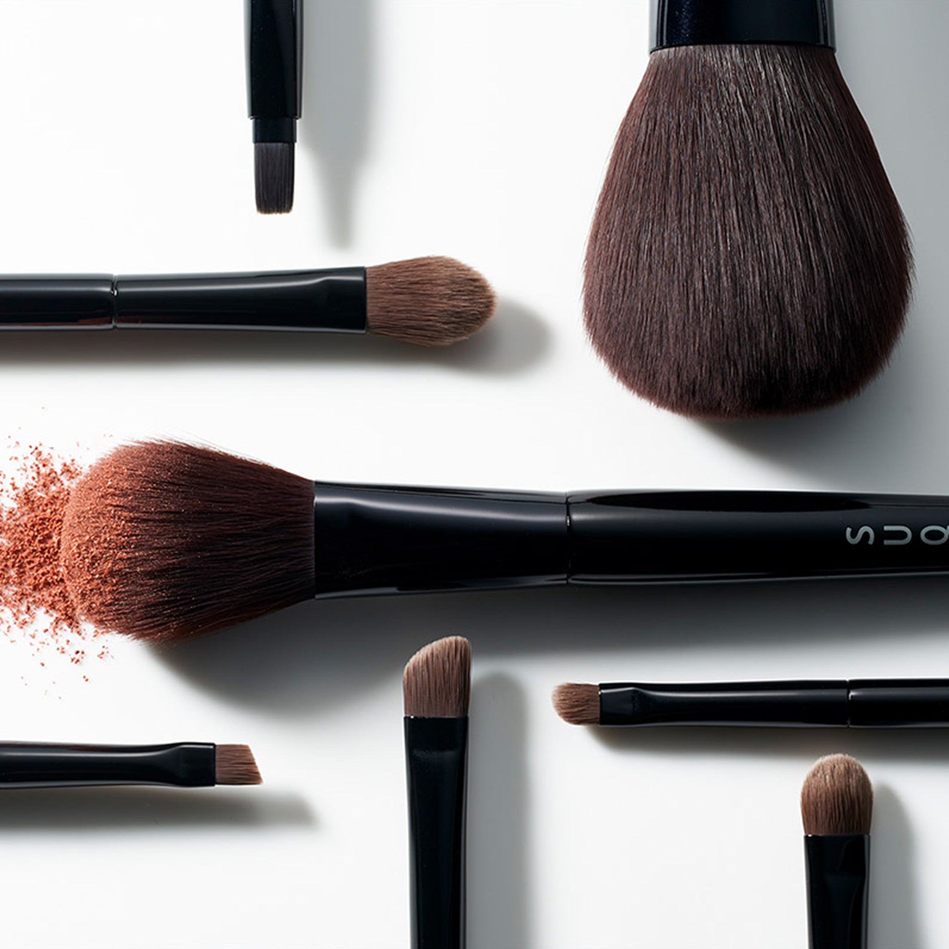 Various SUQQU Japanese synthetic artisan make up brushes on plain background with powder texture bristles.