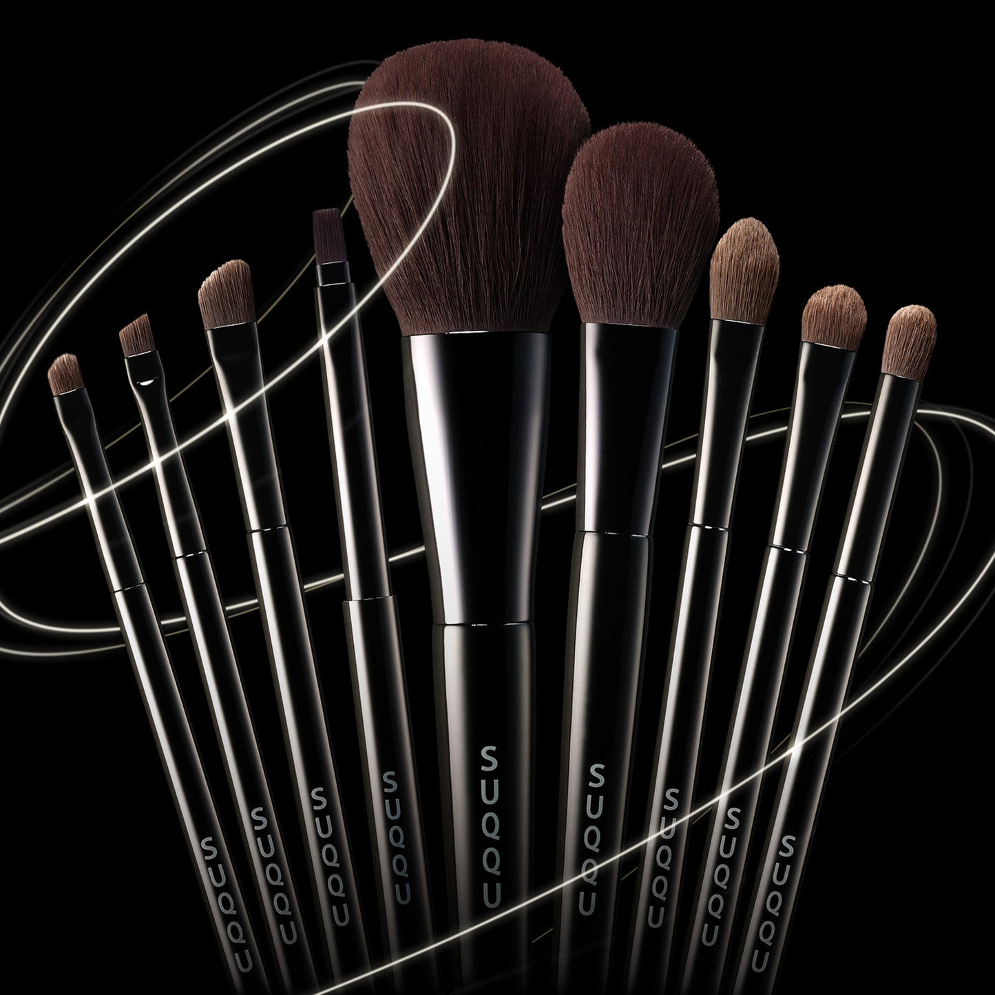 Various SUQQU Japanese synthetic artisan make up brushes grouped on dark background.