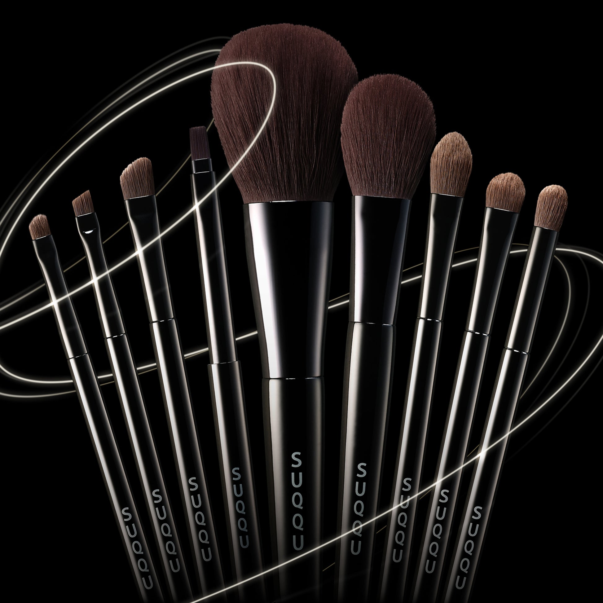Various SUQQU Japanese synthetic artisan make up brushes grouped on dark background.