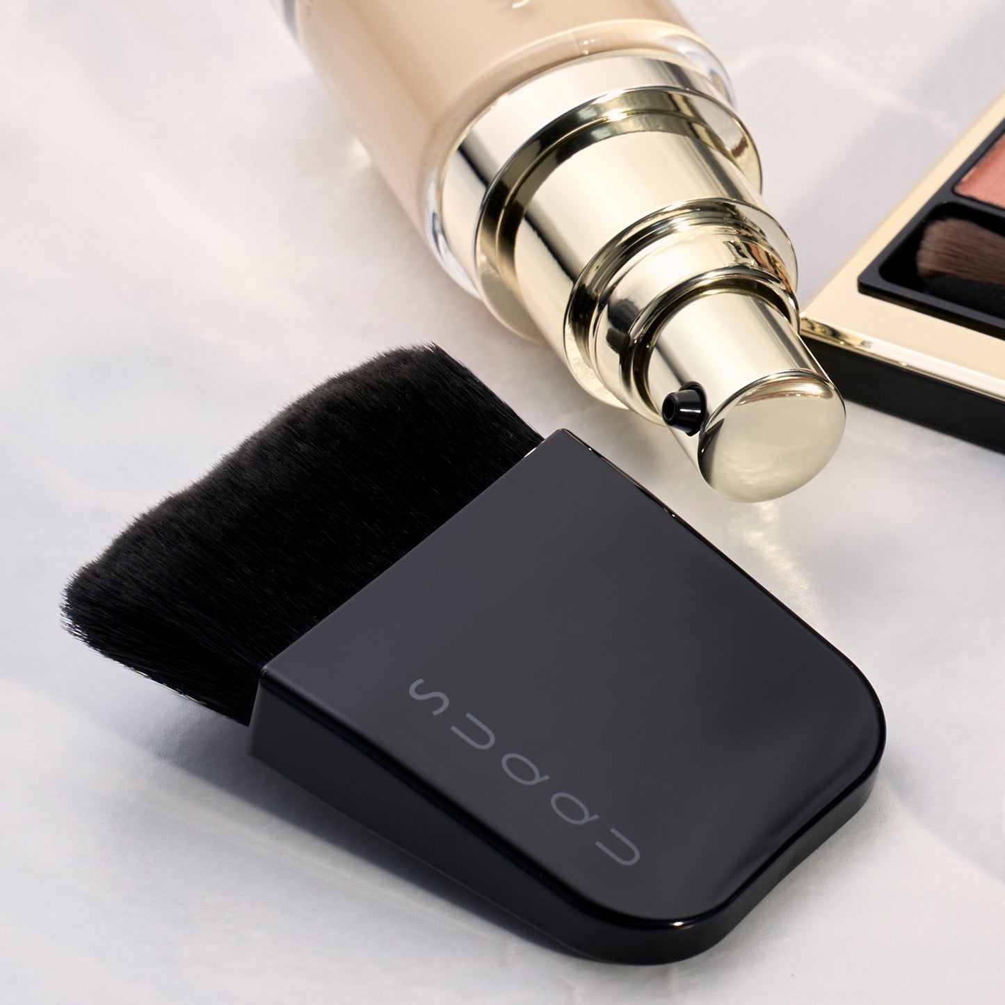 SUQQU Foundation Brush Kabuki style artisan Japanese professional make up brush with foundation and eyeshadow palette on table.