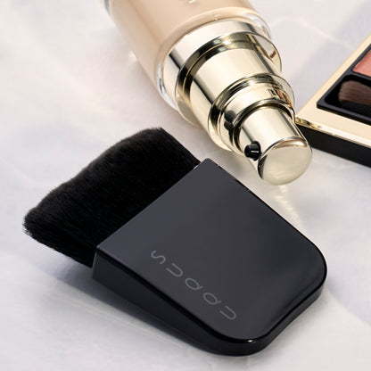 SUQQU Foundation Brush Kabuki style artisan Japanese professional make up brush with foundation and eyeshadow palette on table.
