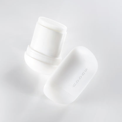 Two SUQQU Glowing Balm products floating on a soft grey background, one is open showing balm stick, the other is closed.