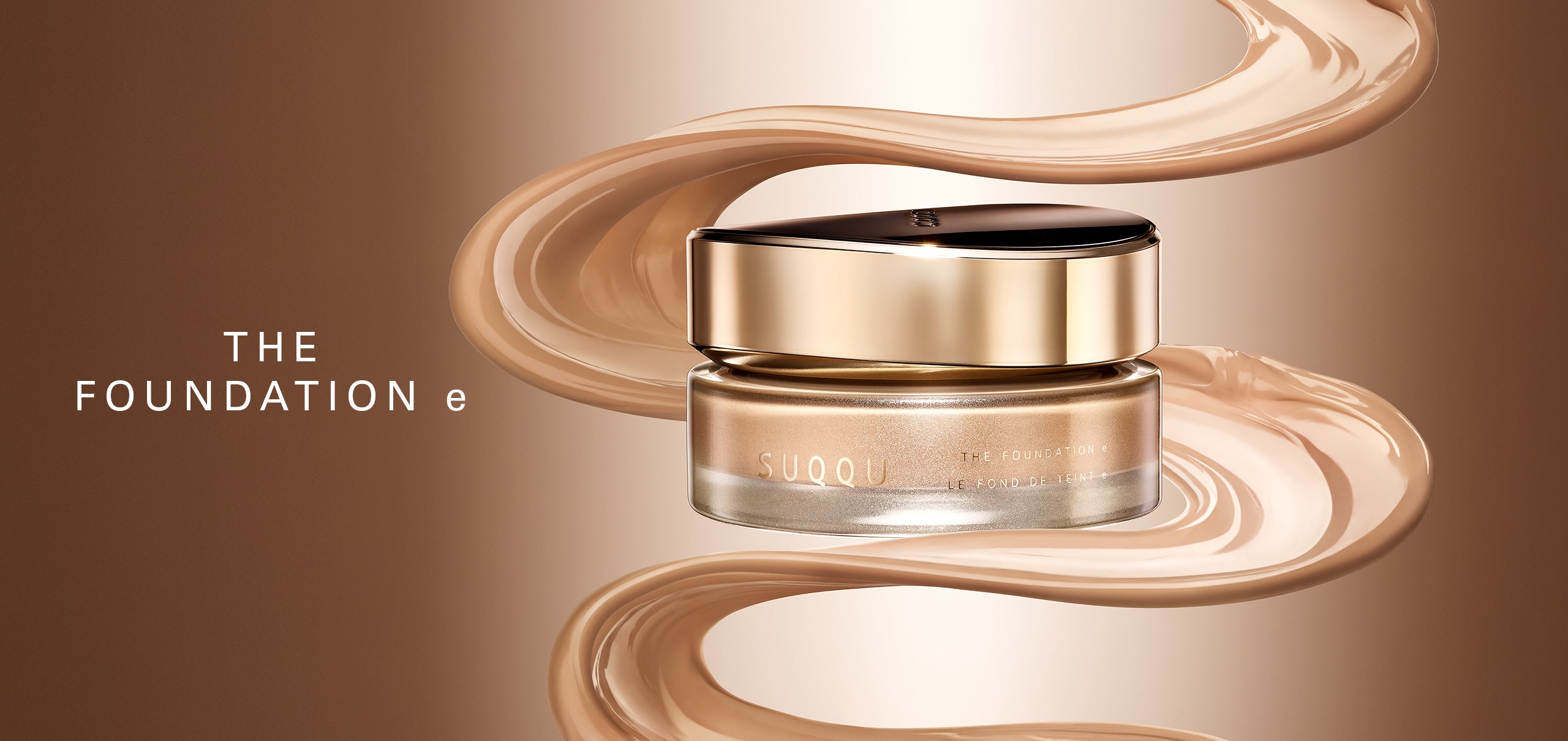 A jar of SUQQU 'The Foundation e' luxury foundation cream is centered against a warm beige gradient background, surrounded by elegant, flowing swirls of the beige foundation cream itself. The jar has a metallic gold lid and a clear glass base showing the cream inside.