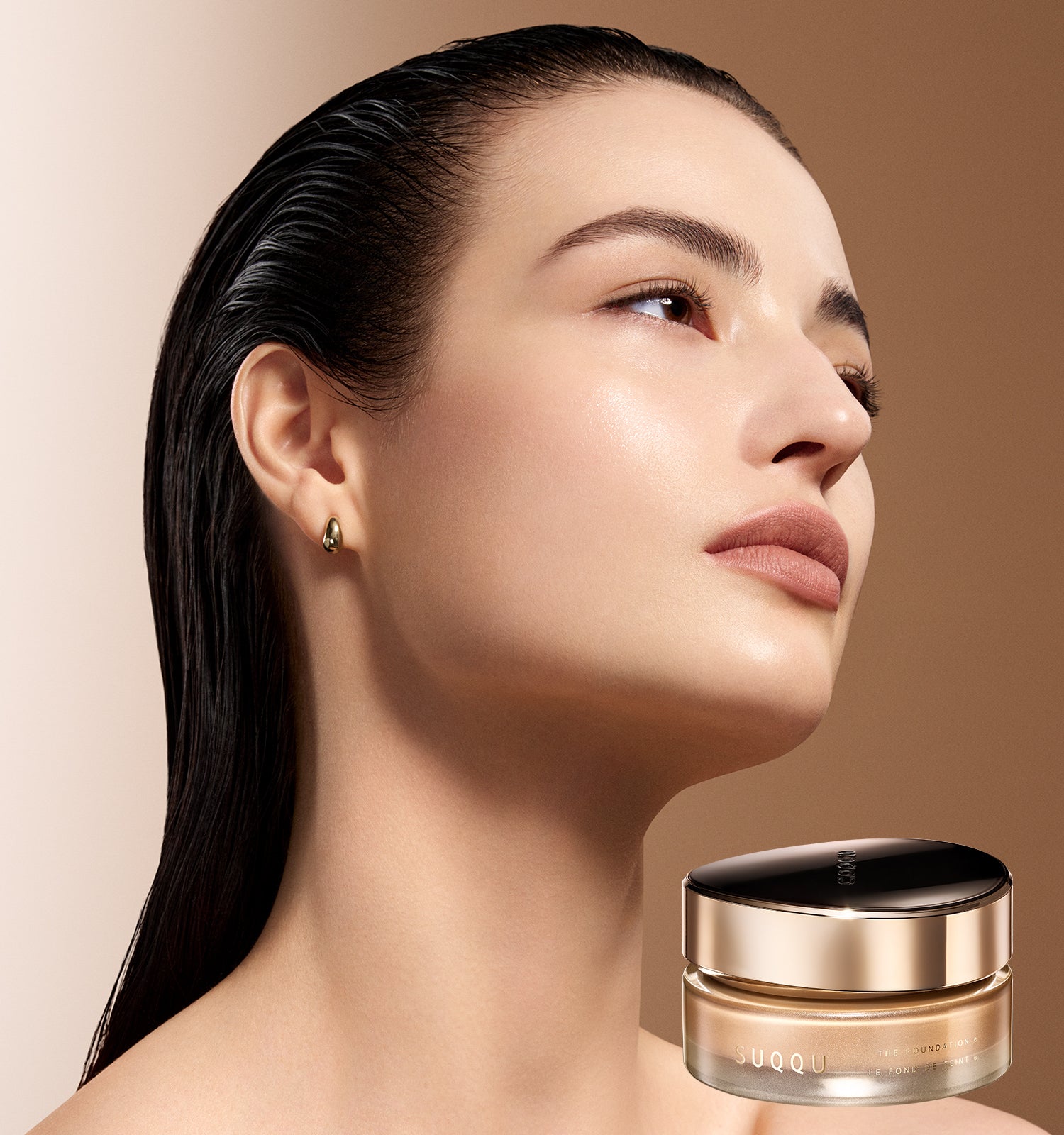 A SUQQU The Foundation e jar with a gold cap on a warm beige background, alongside a close-up of a woman's radiant face complexion.