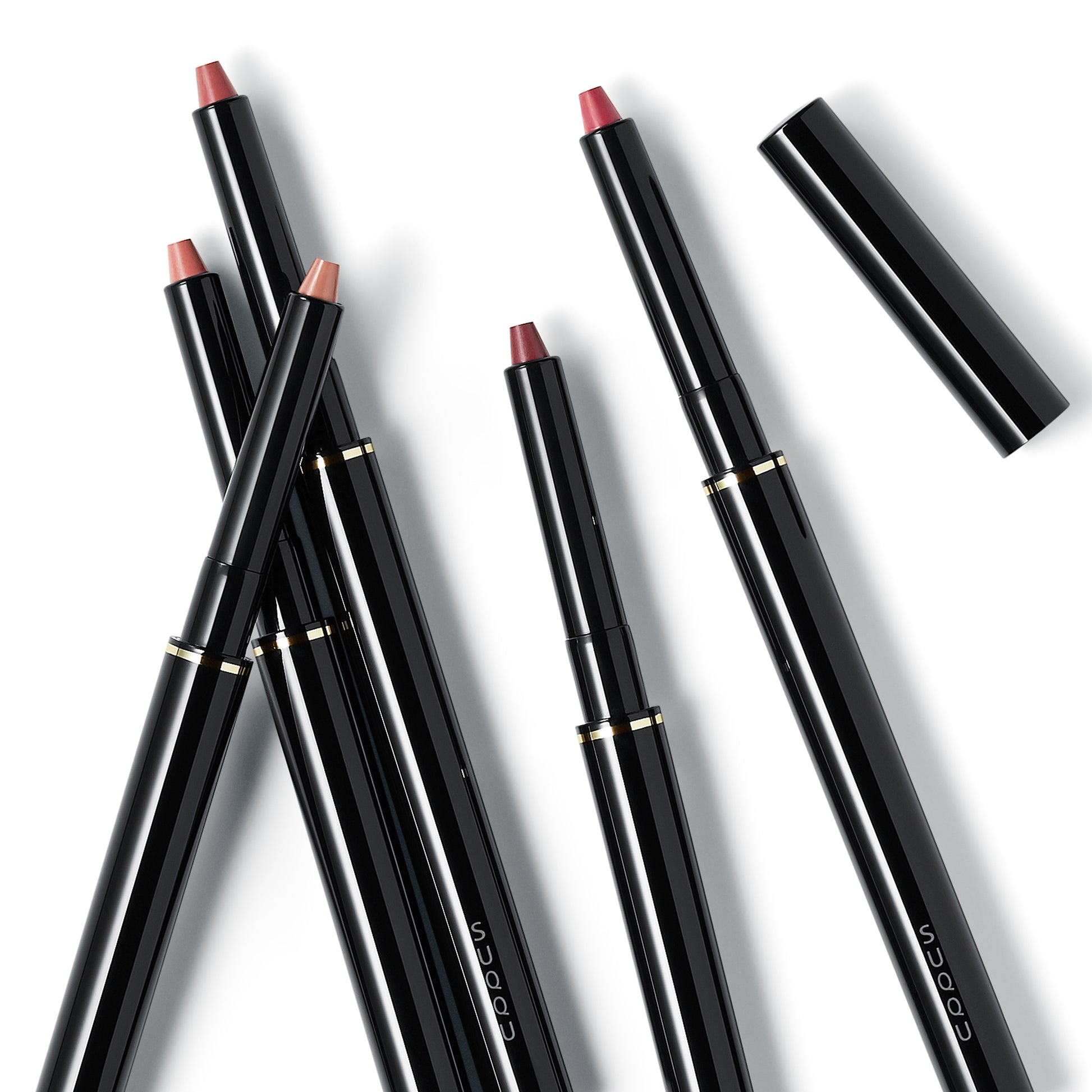 Five shades of SUQQU Lip Defining Pencil product on plain background with cap.