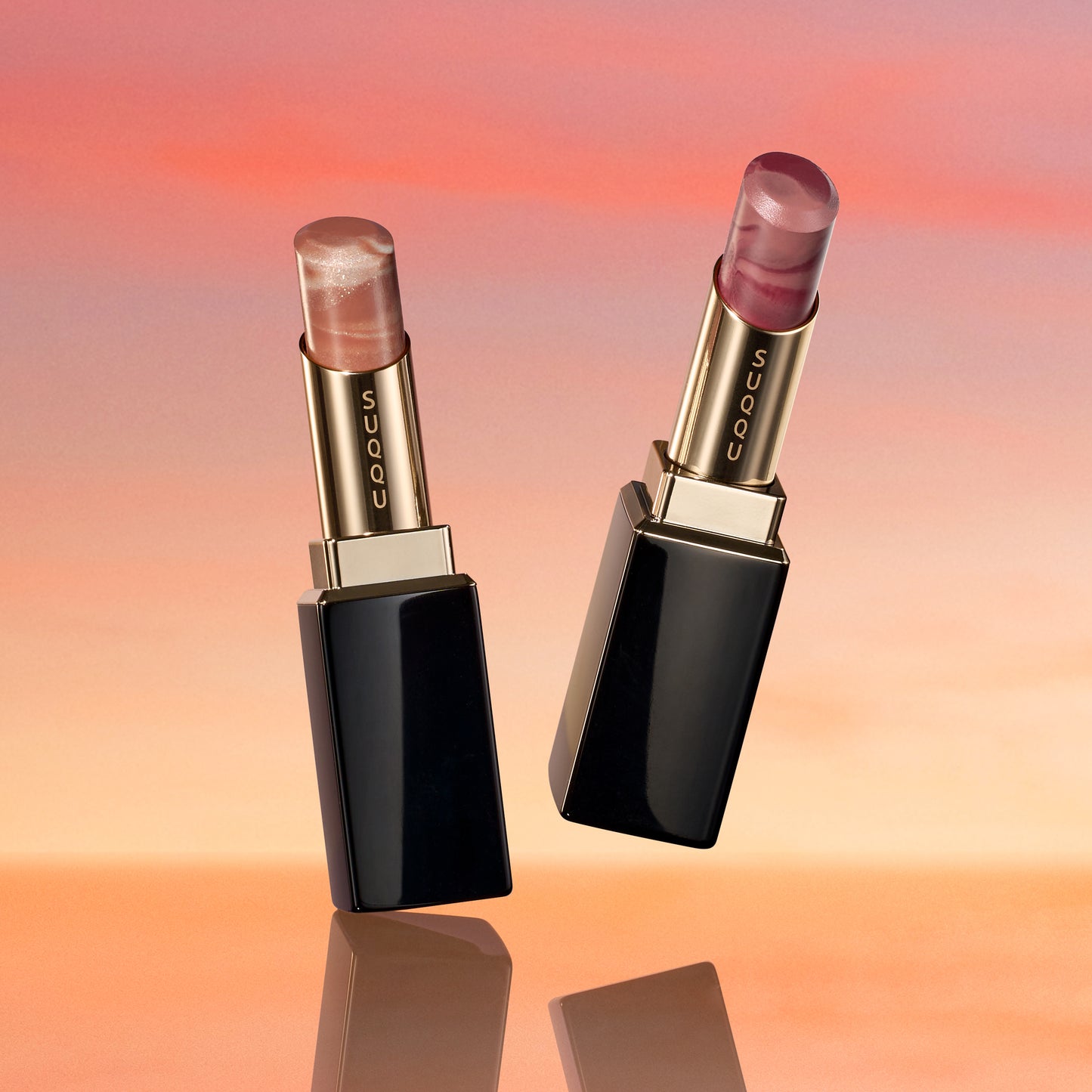 SUQQU 2026 Summer Collection, multiple beautiful colourful luxury makeup products on a gradient sky background. Two lipsticks in orange red and grape red.