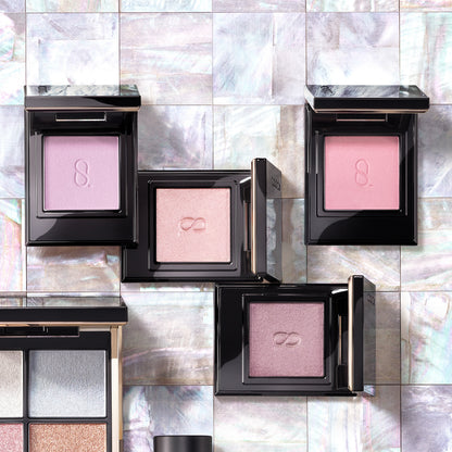 Four beautiful SUQQU Mono Look Eyes single luxury eyeshadow palettes open on a pearl tile table. In pale soft pink and purple, pearlescent glitter and matte finishes.