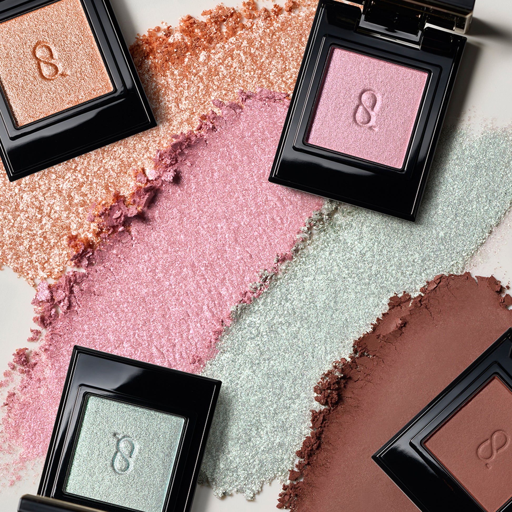 Four SUQQU Mono Look Eyes eyeshadows in four different finishes with coloured textured background.