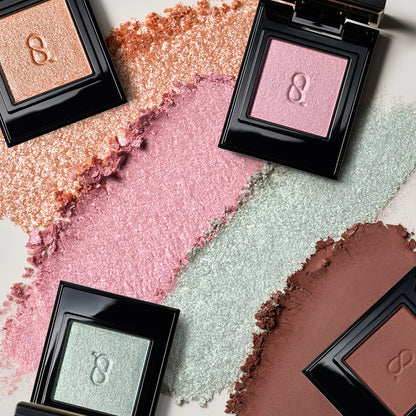 Four SUQQU Mono Look Eyes eyeshadows in four different finishes with coloured textured background.