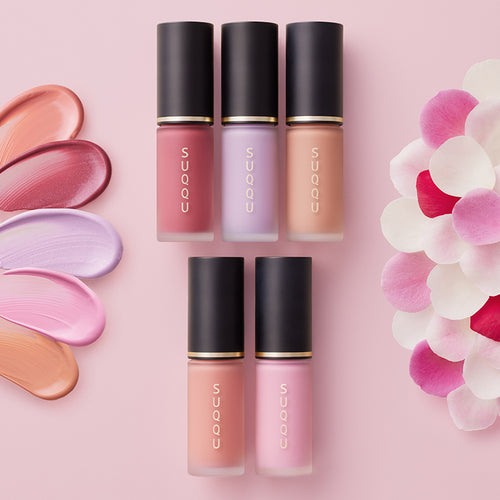 SUQQU Spring Collection 2026 group of five liquid Complexion Face Color makeup product tubes lying on a table arranged with flower petals and colourful texture swatches.