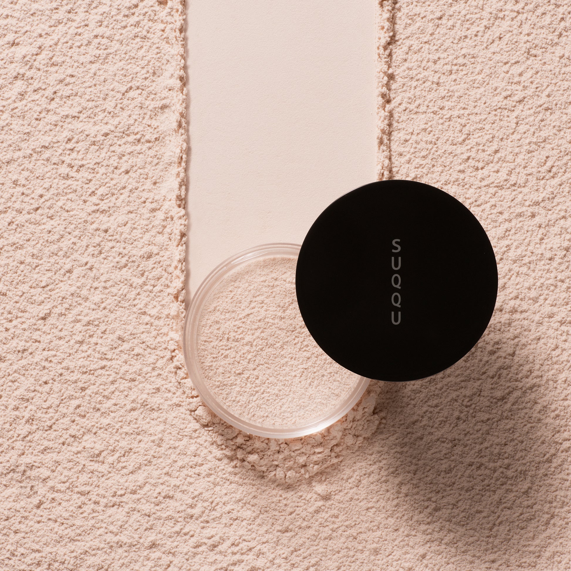 SUQQU Oil Rich Glow Loose Powder e face powder pot on powdery texture background.