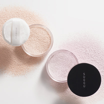 SUQQU Oil Rich Glow Loose Powder e and Sheer Loose Powder e face powder pots on white background with powdery texture.