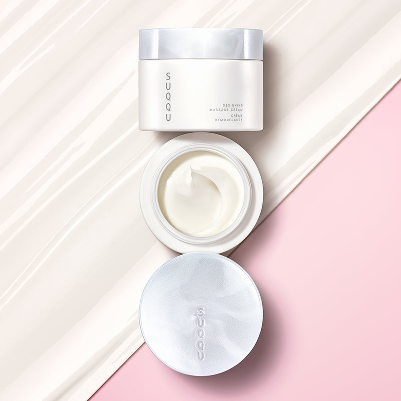 SUQQU Designing Massage Cream skincare tub with lid open on half cream texture background.