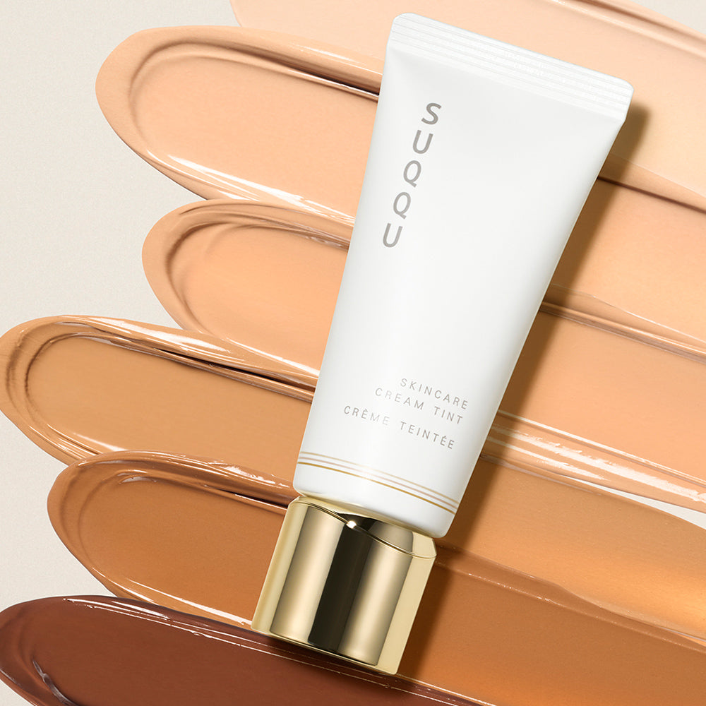 SUQQU Skincare Cream Tint foundation tube with colour texture swatches in the background.