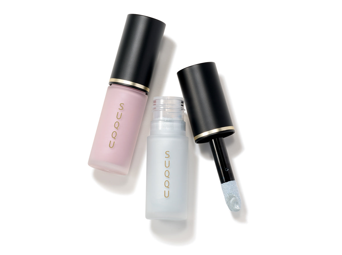 Two SUQQU Complexion Face Color cheek blusher tubes on a table in pale pearl pink and pale shell blue colours. Shown with cap off and applicator wand.