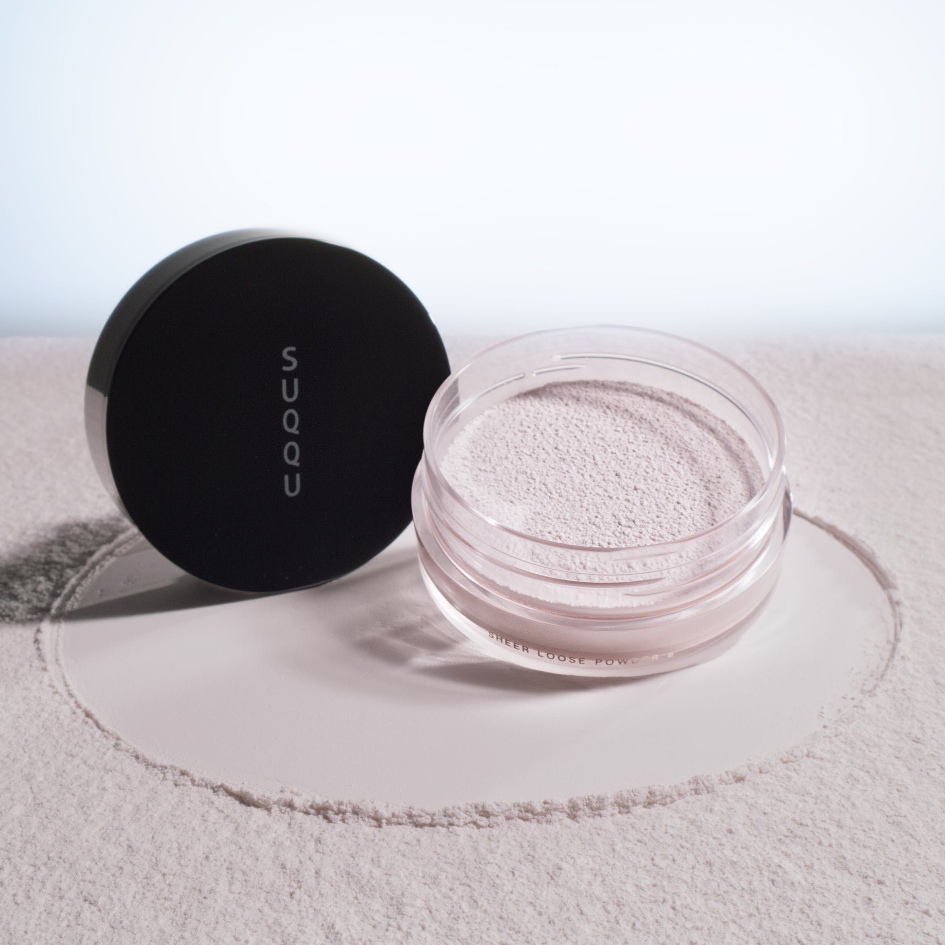 SUQQU Sheer Loose Powder e face powder pot on powdery texture background.