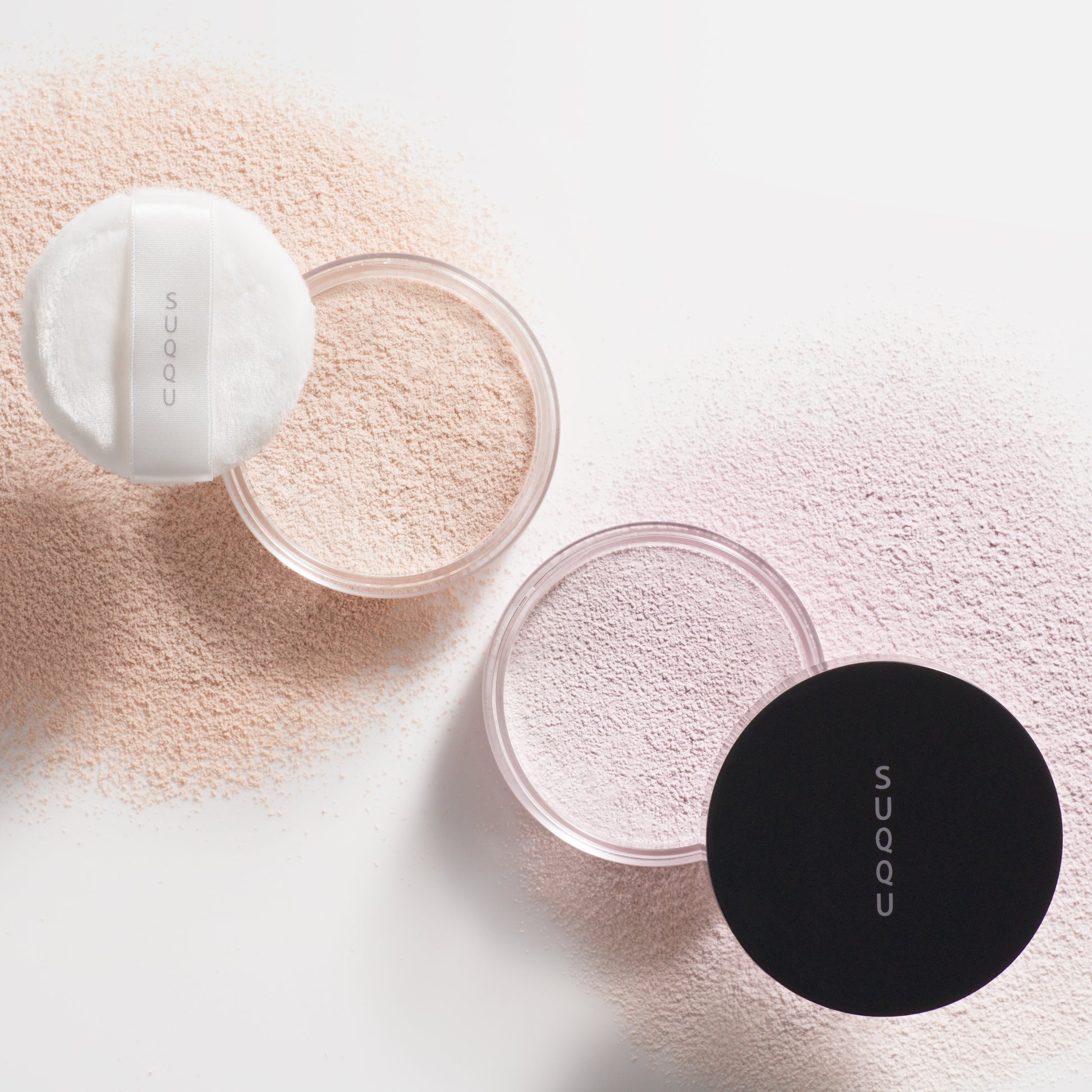 SUQQU Oil Rich Glow Loose Powder e and Sheer Loose Powder e face powder pots on white background with powdery texture.