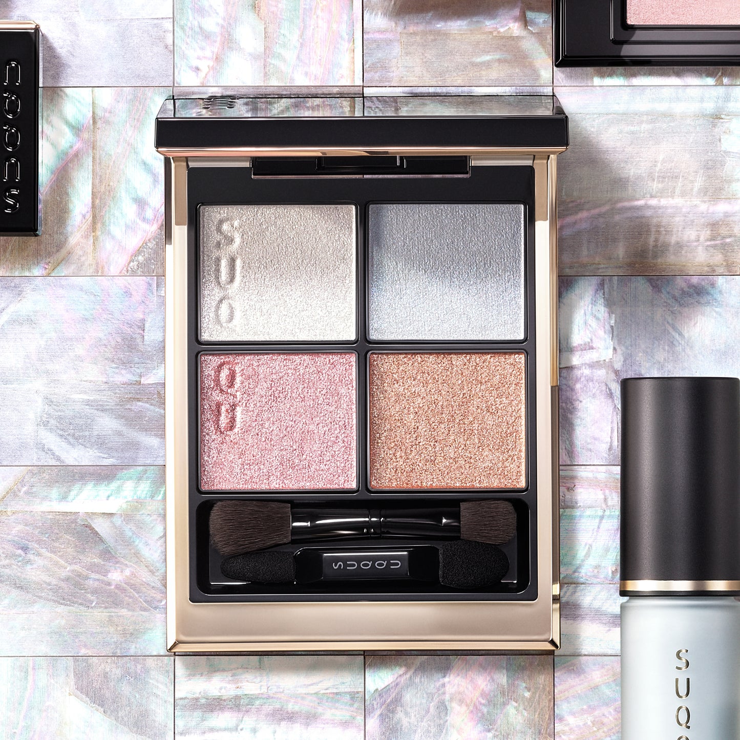 SUQQU Signature Color Eyes 156 gorgeous quad eyeshadow palette on pearl tile background. Pale pink, blue and gold shades with glittering pearl white highlighter. Surrounded by other makeup products.