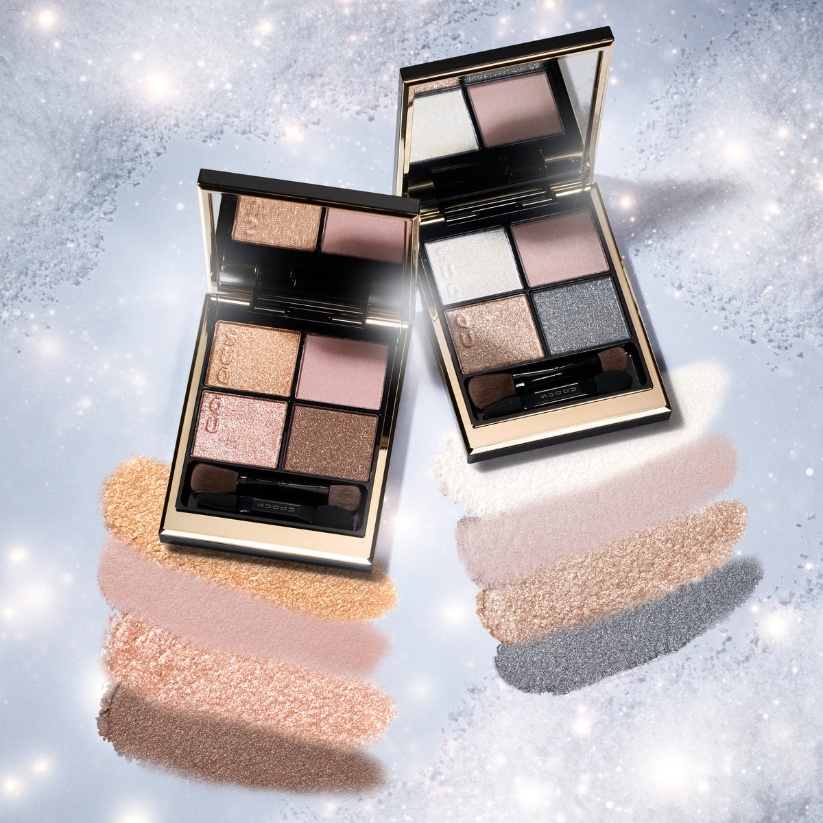 Two SUQQU Signature Color Eyes 157 & 158 open four-pan eyeshadow palettes with matching applicators, displayed on a sparkly light blue background with shimmer swatches beneath each pan. The palettes have black and gold packaging with neutral and shimmery shades in beige, pink, brown, gray, and white.