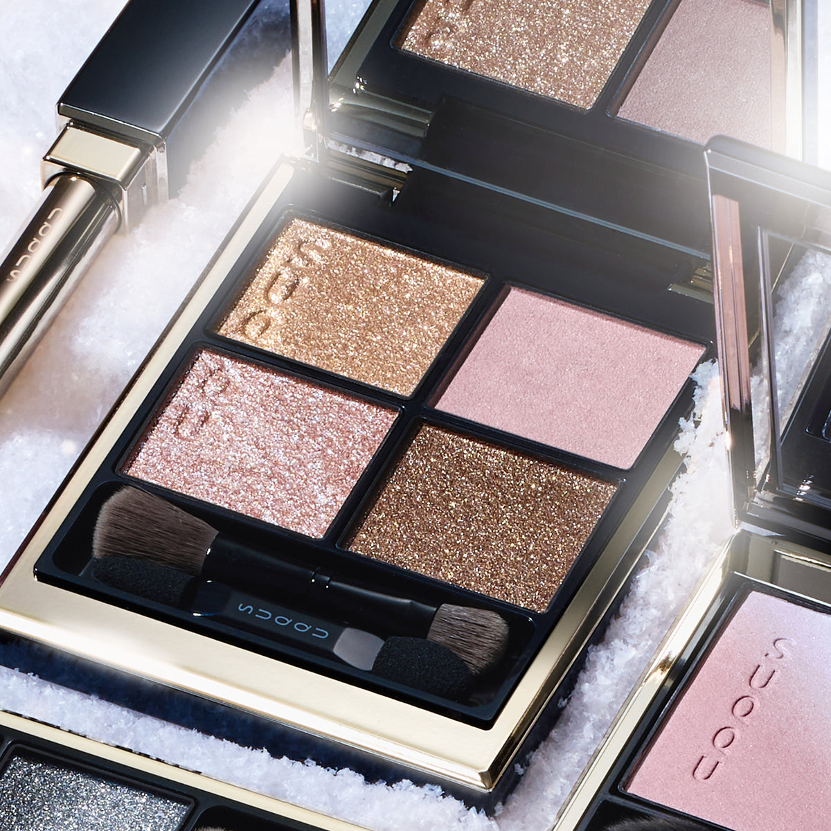 SUQQU Signature Color Eyes 157 luxury Japanese cosmetic quad eyeshadow compact close up on a snowy background with other collection products. Coral pink and pale beige pink with gold and brown.