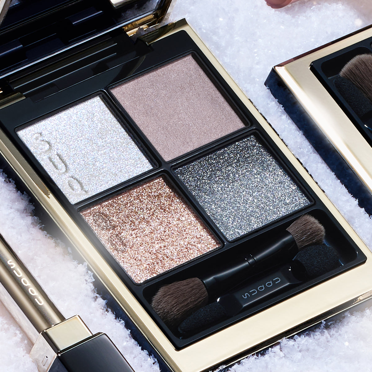 SUQQU Signature Color Eyes 158 luxury Japanese cosmetic quad eyeshadow compact close up on a snowy background with other collection products. Dusty pink and pale beige pink with light blue and dusty navy blue. Fine textured pearl glitter and creamy skincare ingredients.