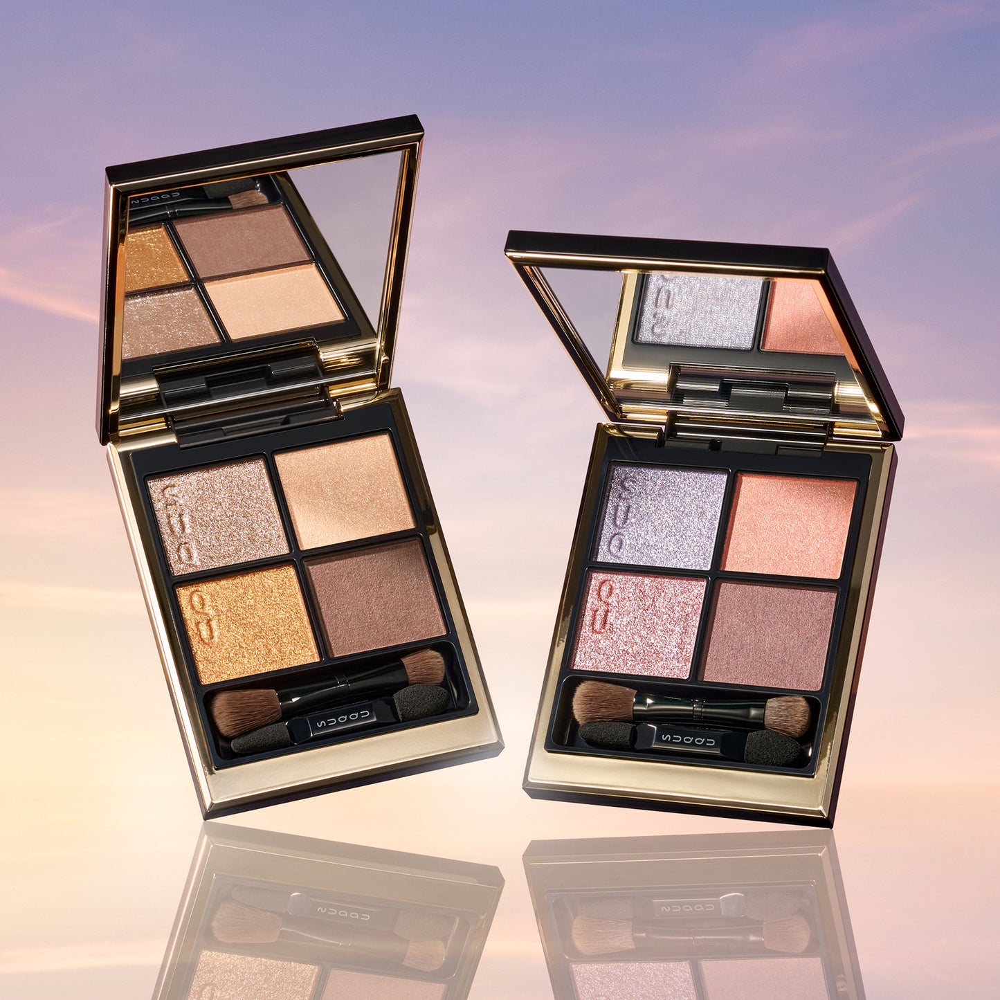 SUQQU 2026 Summer Collection, multiple beautiful colourful luxury makeup products on a gradient sky background. Two eyeshadows with gold and pink coral tones.