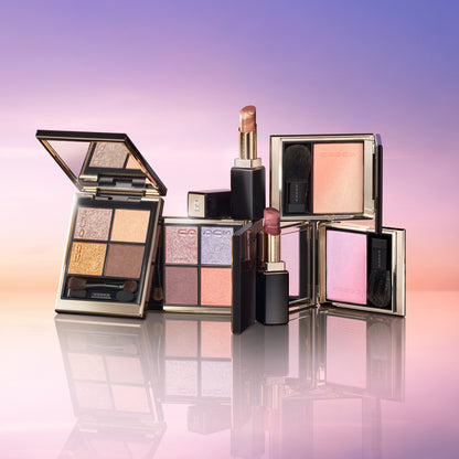 SUQQU 2026 Summer Collection, multiple beautiful colourful luxury makeup products on a gradient sky background. Two eyeshadows with gold and pink coral tones, two blushers with organe gold and lilac pink and two lipsticks in orange red and grape red.