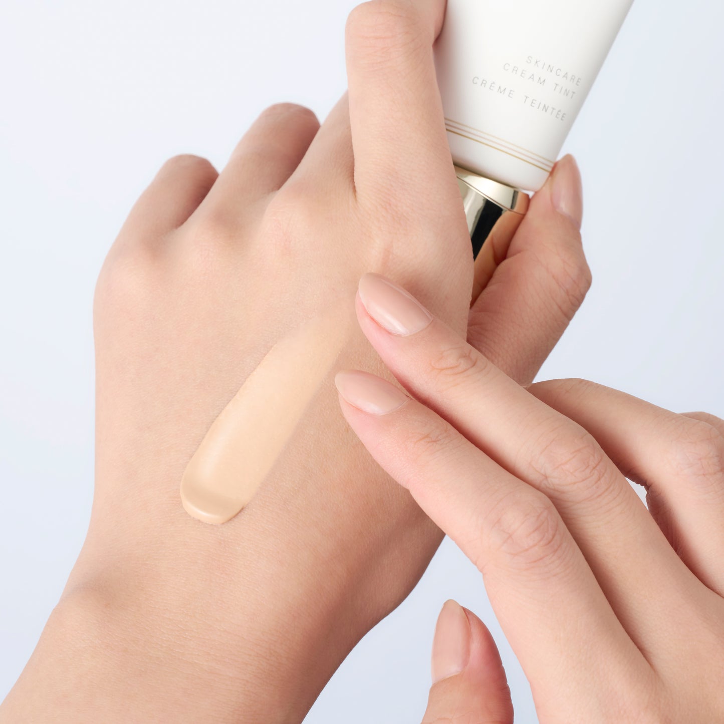 SUQQU Skincare Cream Tint skincare based light liquid foundation swatch applied to the back of a models hand whilst holding the tube product.